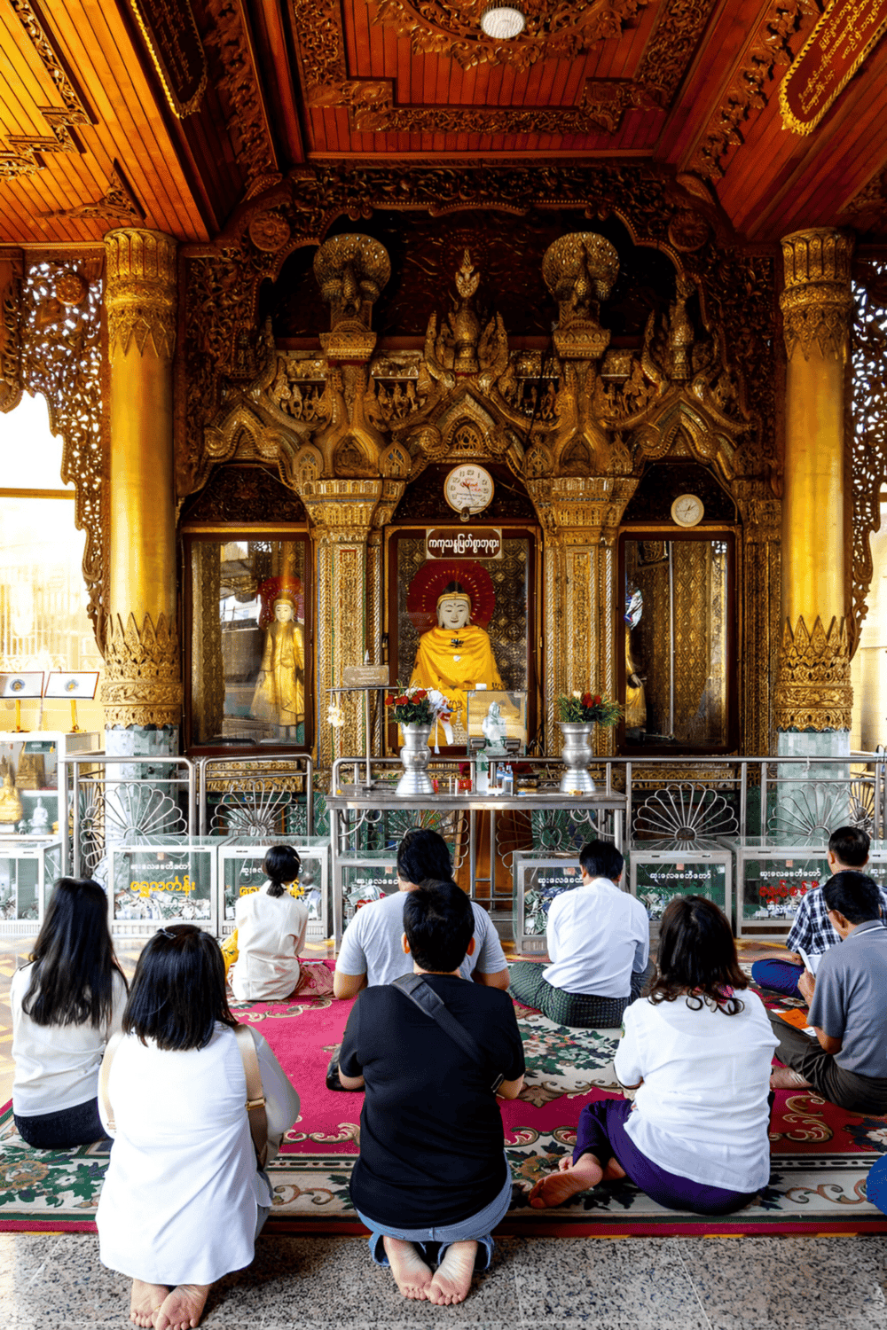 Altar with golden wood carvings in a Buddhist temple, people praying, Myanmar cultural site, spiritual worship, religious ceremony.