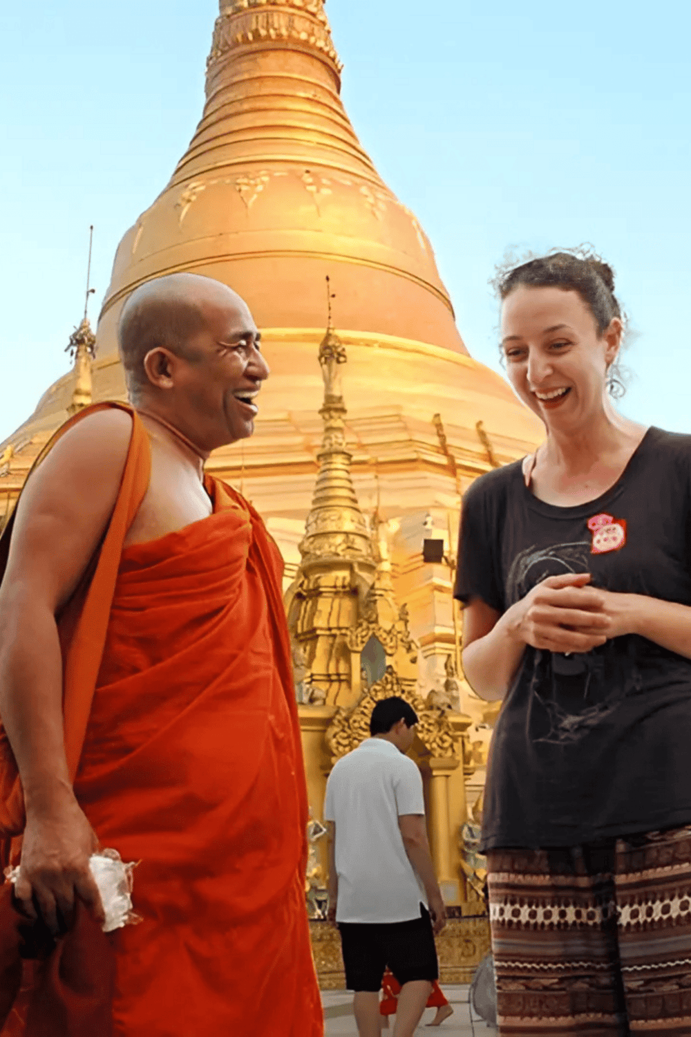 Traditional Thai Buddhist monk smiling with a tourist in front of a golden pagoda in Thailand.