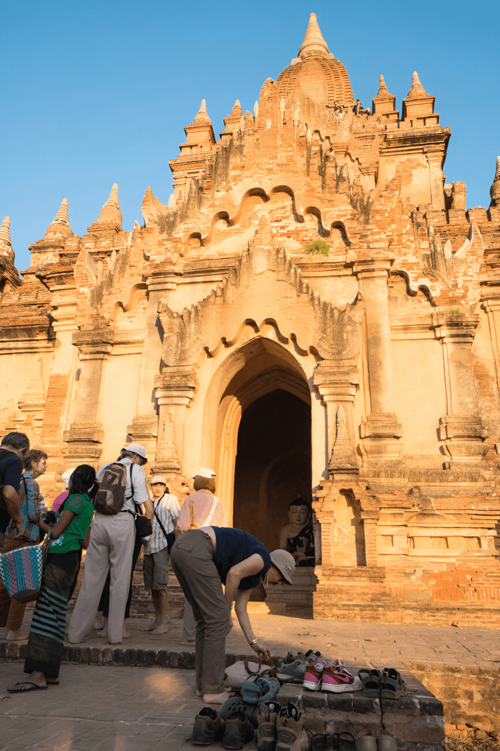 Ancient temple with tourists and shoes outside in Thailand, showcasing cultural heritage and historic architecture.