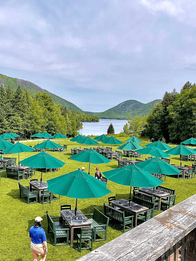Aluminum umbrellas with outdoor dining tables overlooking a scenic lake and mountain landscape.