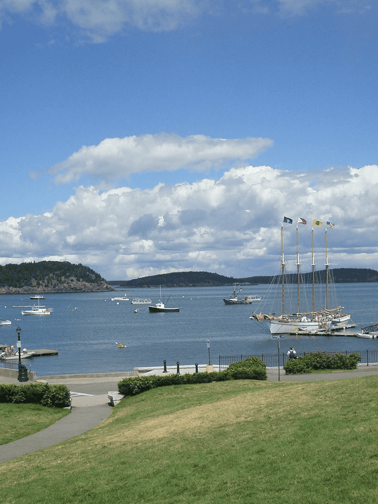 Coastal harbor with boats and sailing ships under cloudy sky, scenic seaside view for travel and navigation.