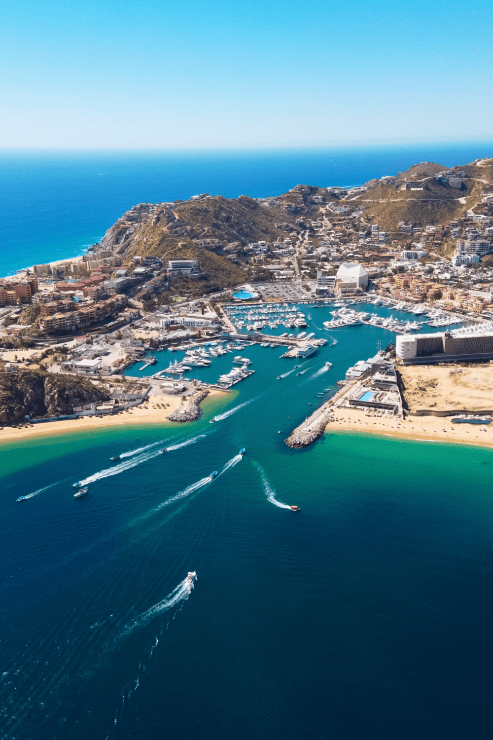 Vibrant aerial view of a luxurious marina and coastal cityscape with boats, hills, and turquoise waters.