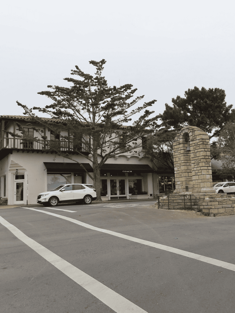 Modern shopping center with luxury retail stores and a historic monument in a quaint town setting.