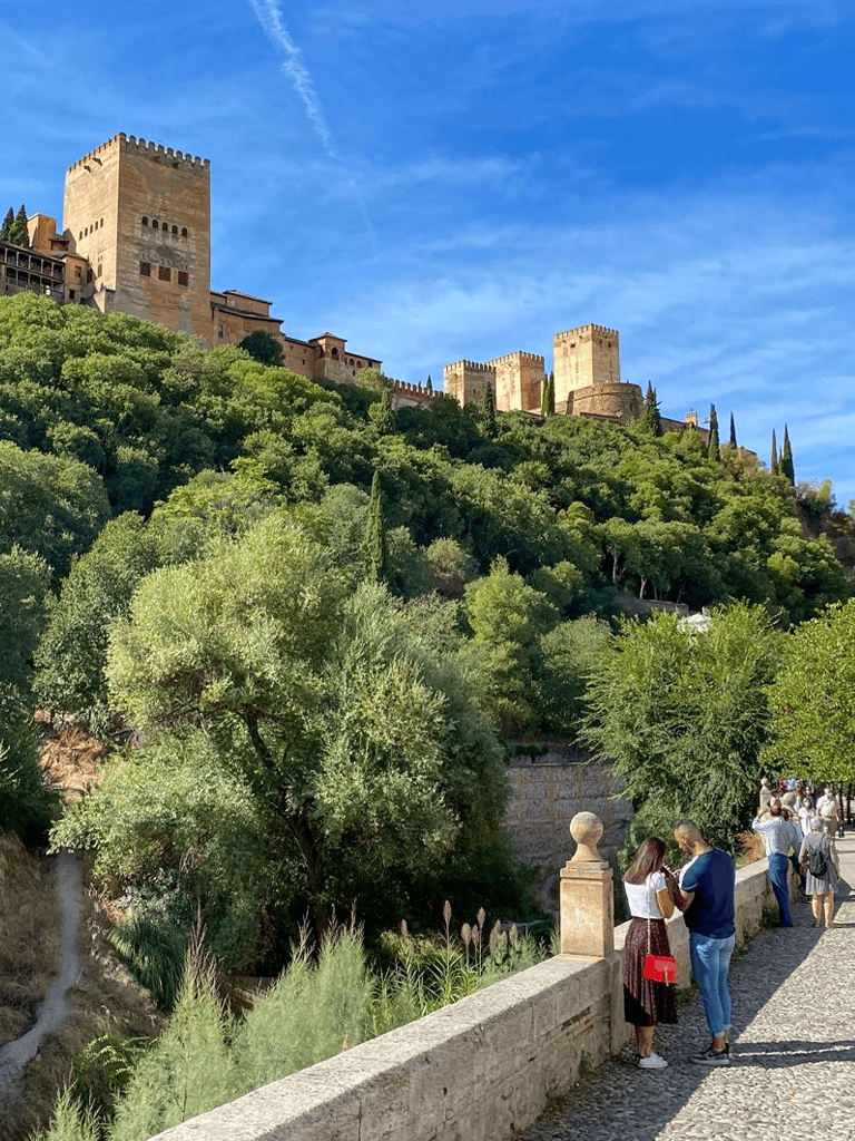 Ancient Alhambra Palace in Granada Spain overlooking lush greenery and a lively tourist scene.