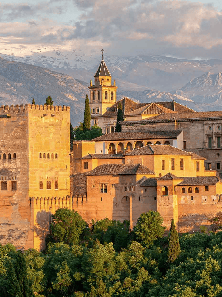 Ancient Alhambra Palace in Granada Spain with mountain backdrop, historic architecture, and lush greenery.