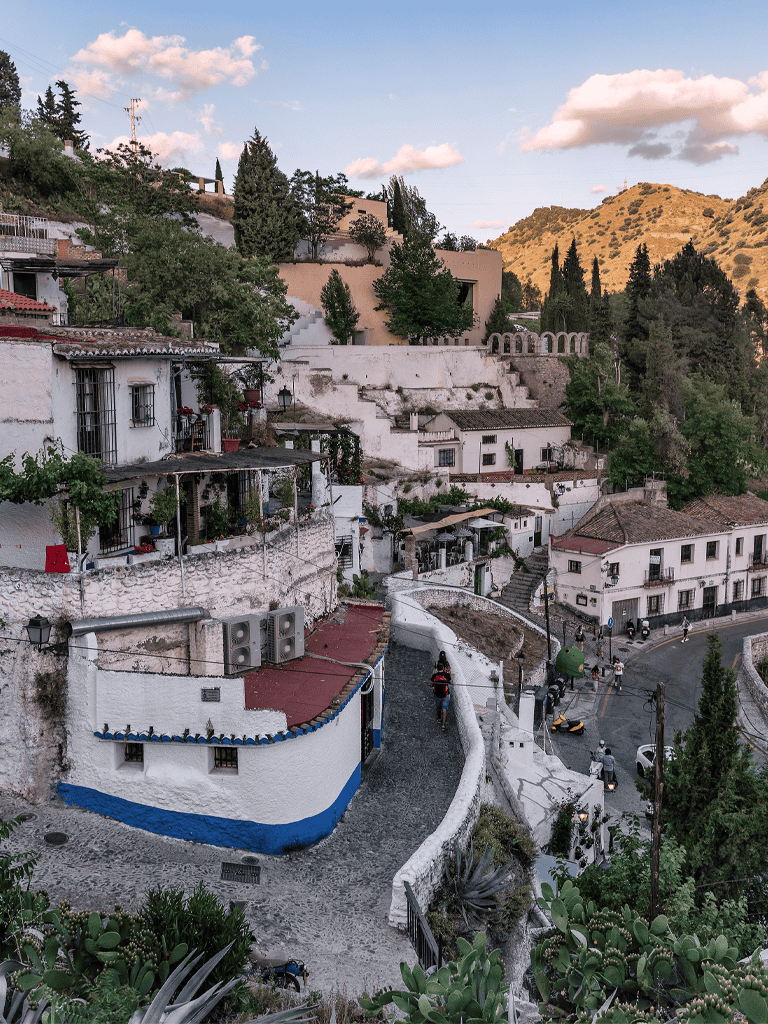 Steep hillside village with white buildings, terraced stairs, and lush greenery in a mountainous region.