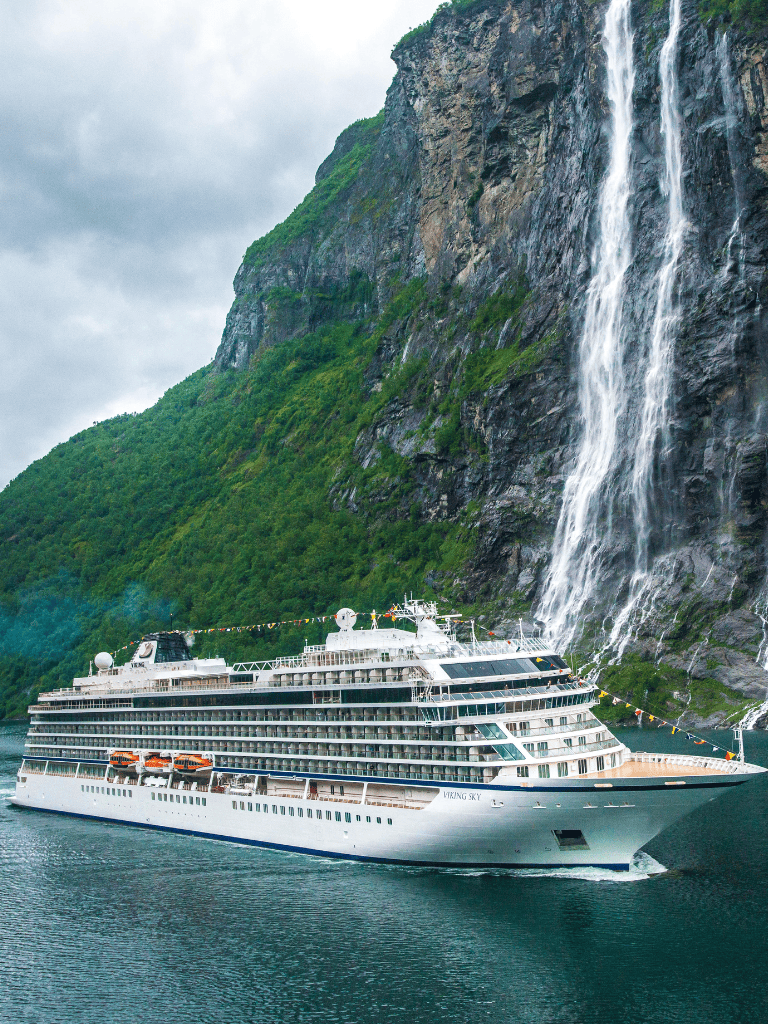 Luxurious cruise ship sailing near stunning fjord with waterfall landscape in Norway.