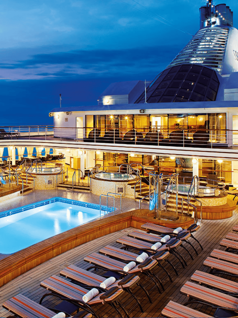 Luxurious cruise ship deck with pool and sun loungers at dusk, perfect for relaxing and scenic ocean views.