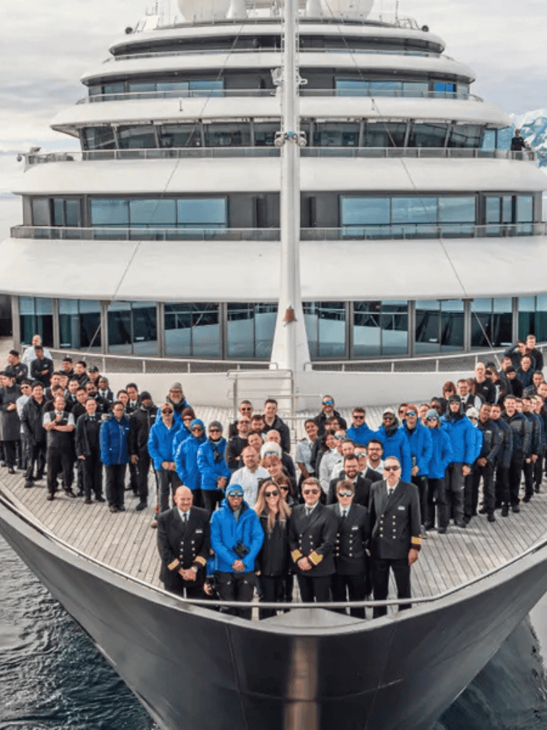 Luxury cruise ship with crew and passengers on deck, scenic ocean voyage.