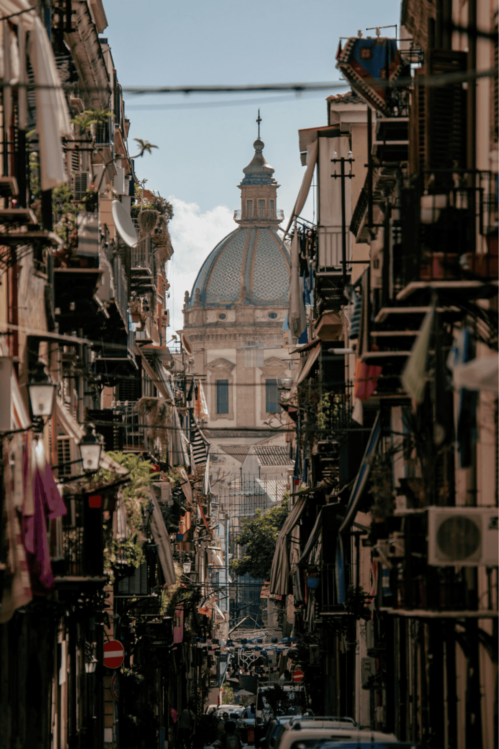 Pastel-colored buildings with balconies, narrow street, and iconic church dome in Palermo, Italy.