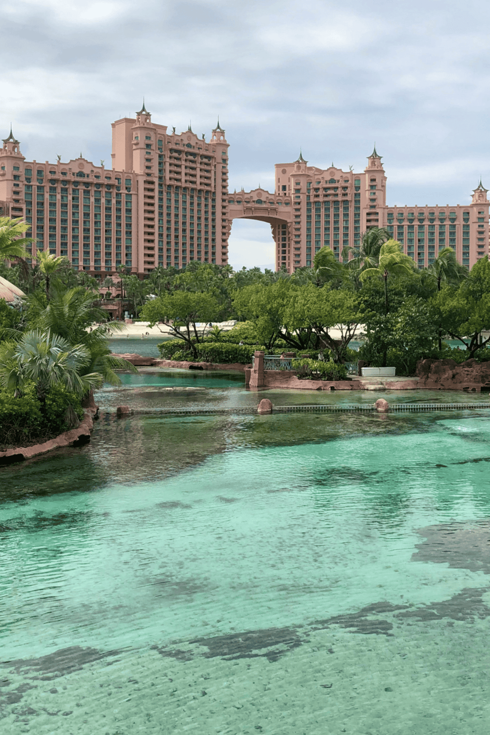 Pink hotel with water park in the foreground, lush greenery, and tropical landscaping.