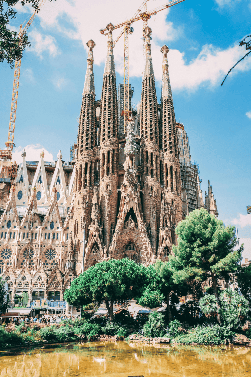 Majestic Sagrada Familia Cathedral in Barcelona, under construction, with blue sky and lush greenery in foreground.
