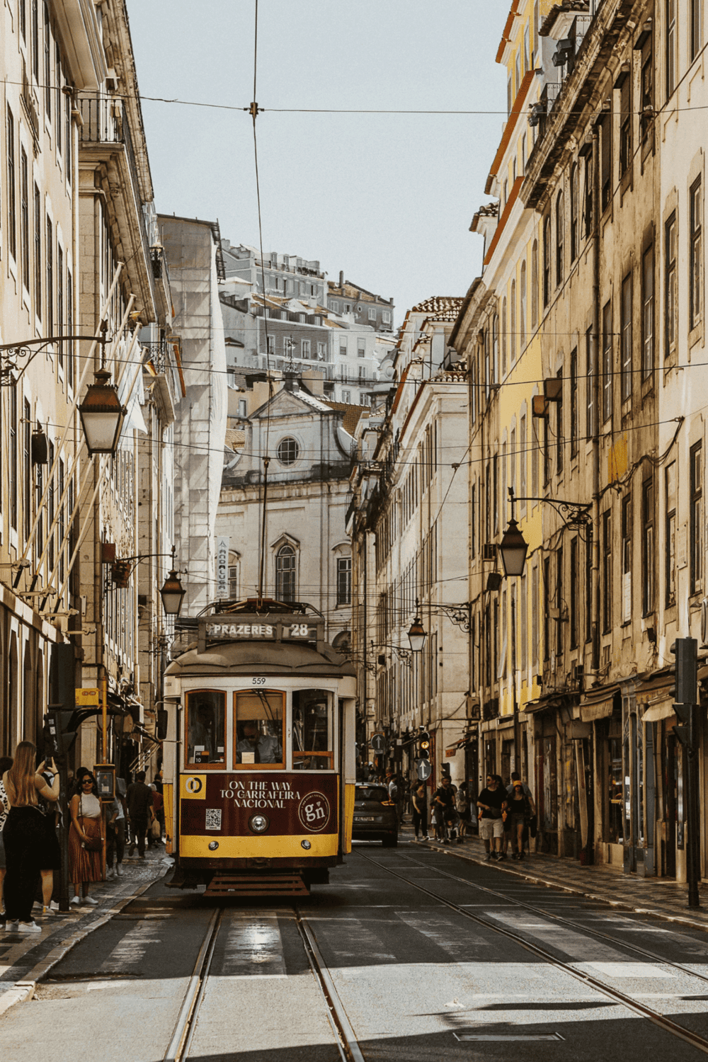 A vintage tram on a narrow street in Lisbon, Portugal, surrounded by historic buildings and busy pedestrians.