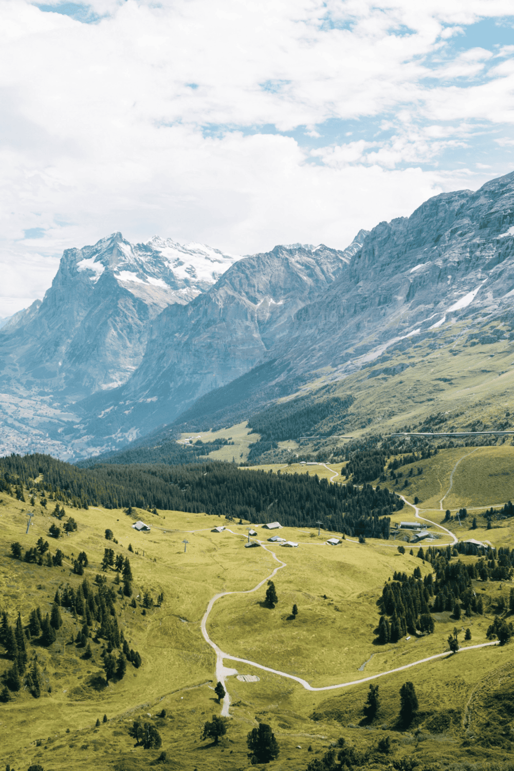 Serene mountain landscape with lush green hills and winding trails near snow-capped peaks.