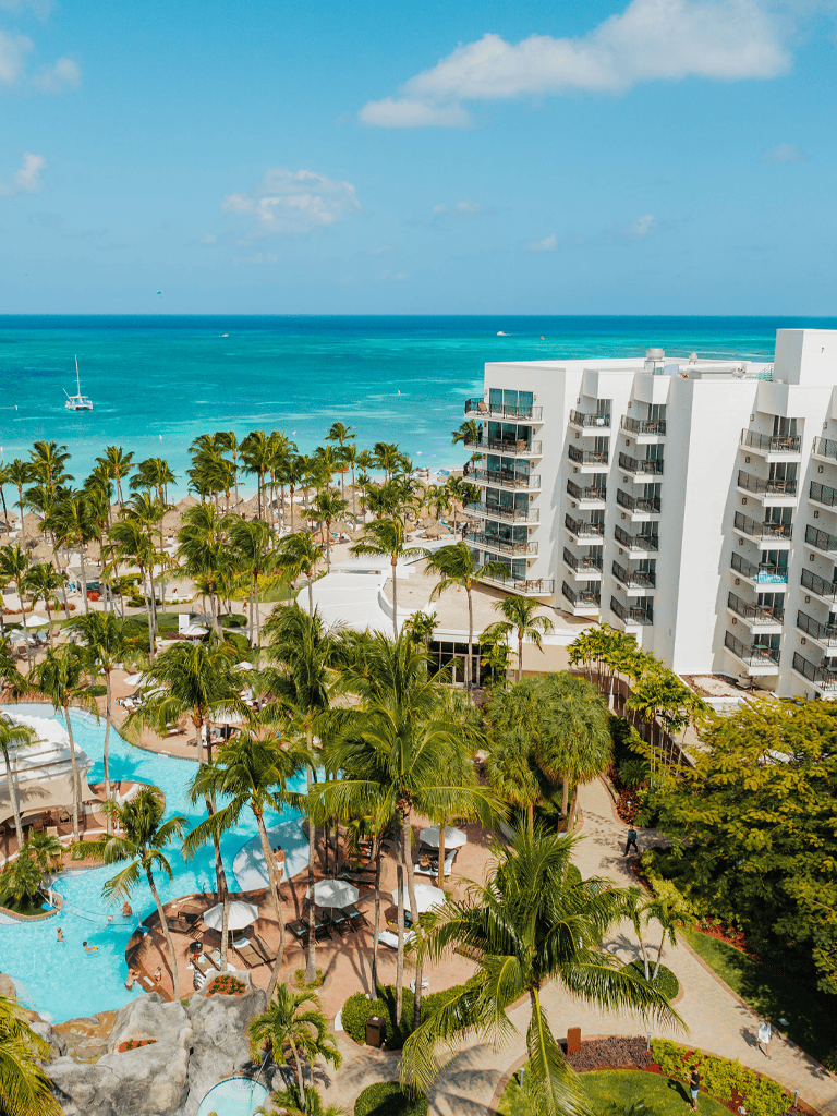 Beachfront hotel with swimming pool, ocean view, tropical palm trees, modern amenities, and vacation-ready atmosphere.