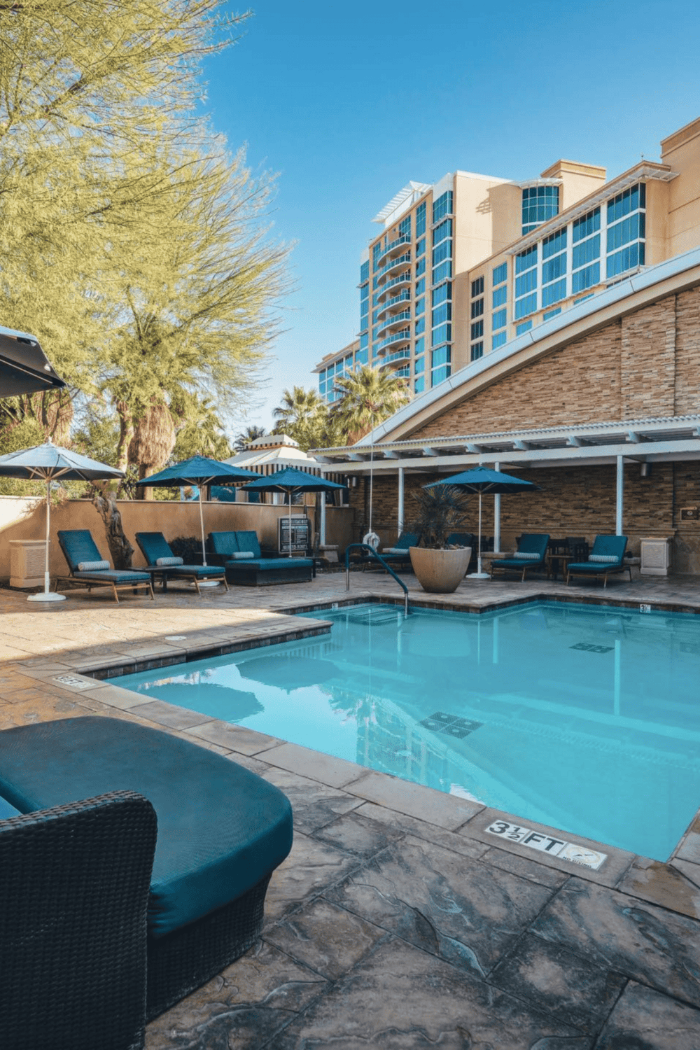 Relaxing hotel pool area with lounge chairs and umbrellas in front of modern high-rise buildings.