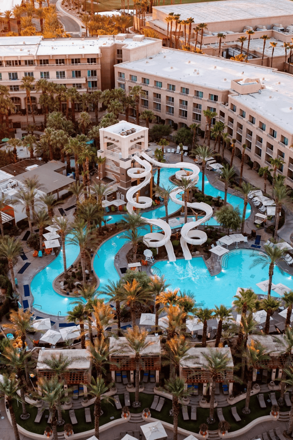 3 water slides at a luxurious resort swimming pool with palm trees and lounging areas.