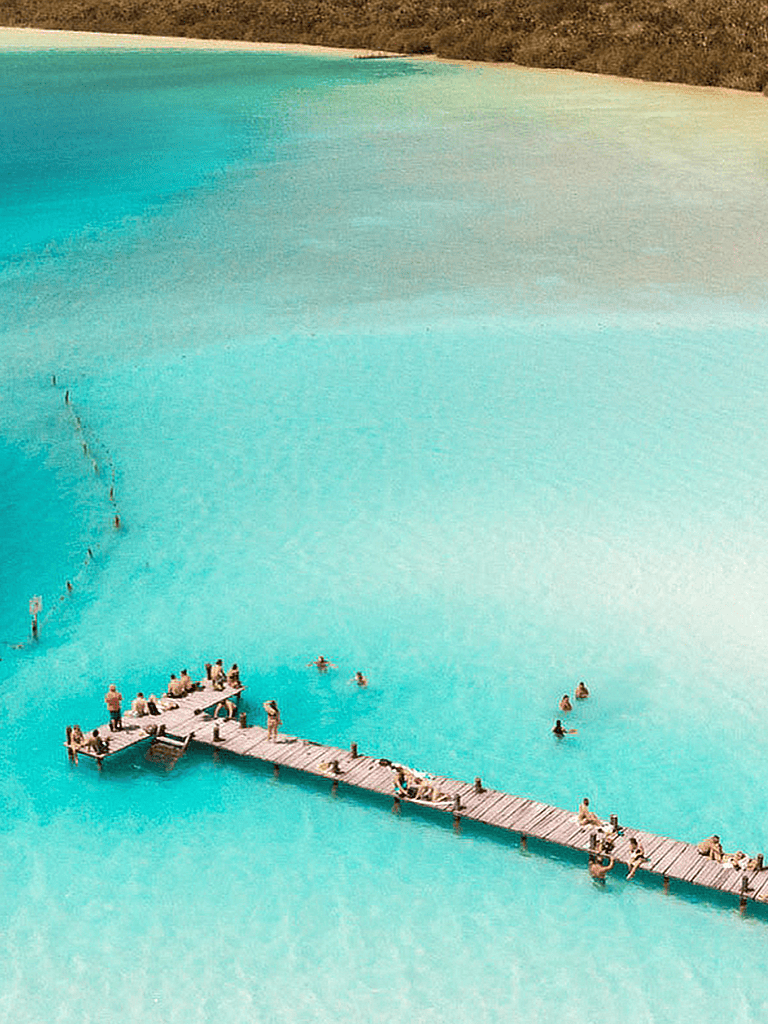 Serene turquoise lagoon with a wooden dock and people enjoying swimming and relaxing.