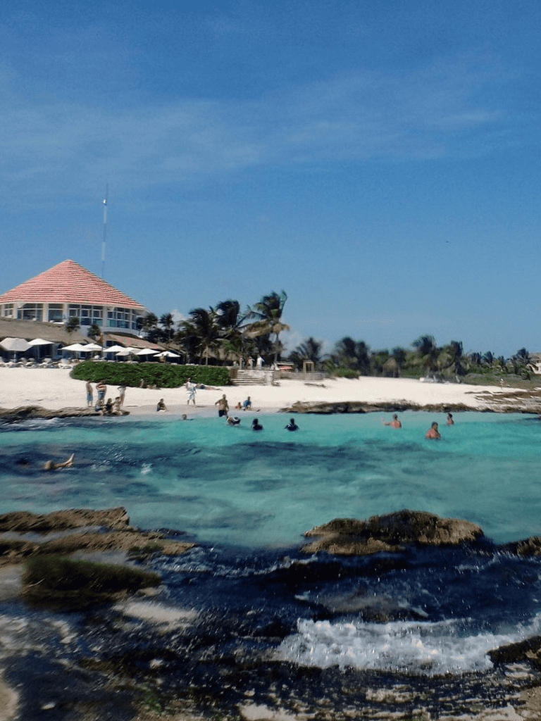 Relaxing beach scene with turquoise waters, palm trees, and a beachfront restaurant, showcasing a sunny island getaway.