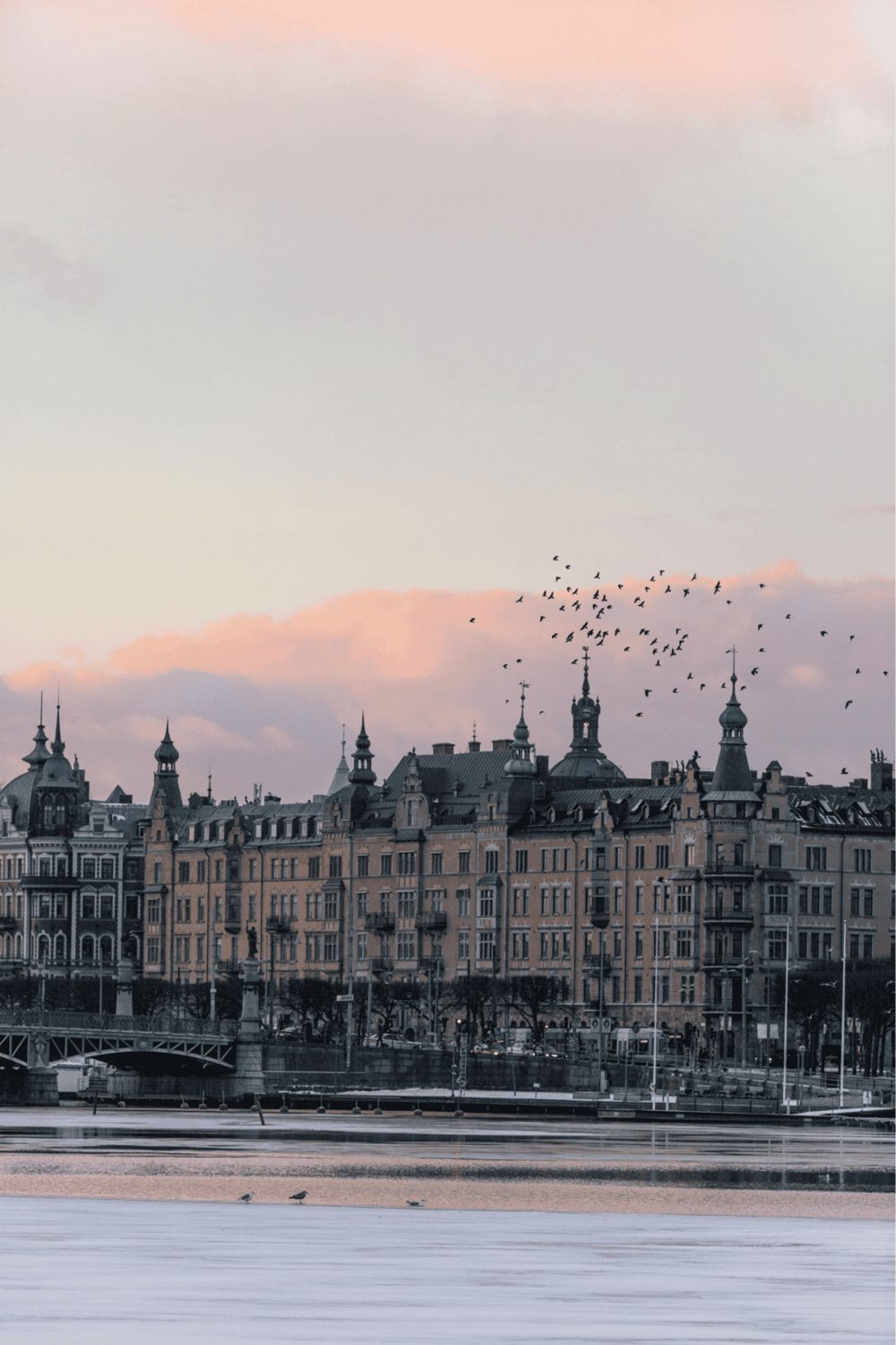 Ancient European cityscape with historic architecture and a waterfront view at sunset.