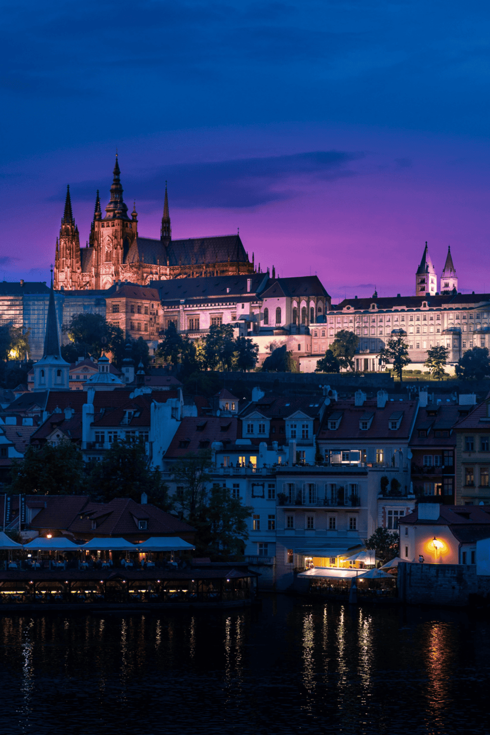 Historic Prague Castle illuminated at night, showcasing gothic architecture and scenic city views.