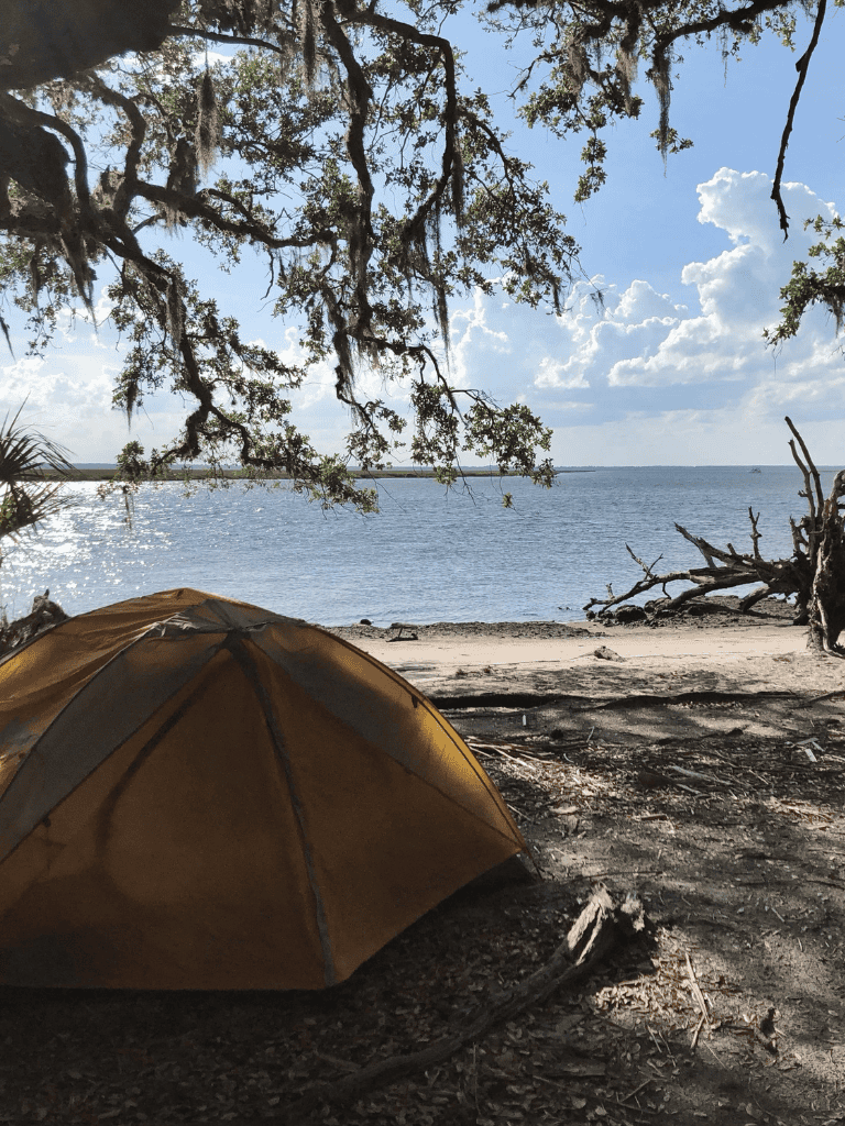 Tent camping by the water with trees and sky in the background, outdoor gear, adventure, nature exploration, QuestForDirections.