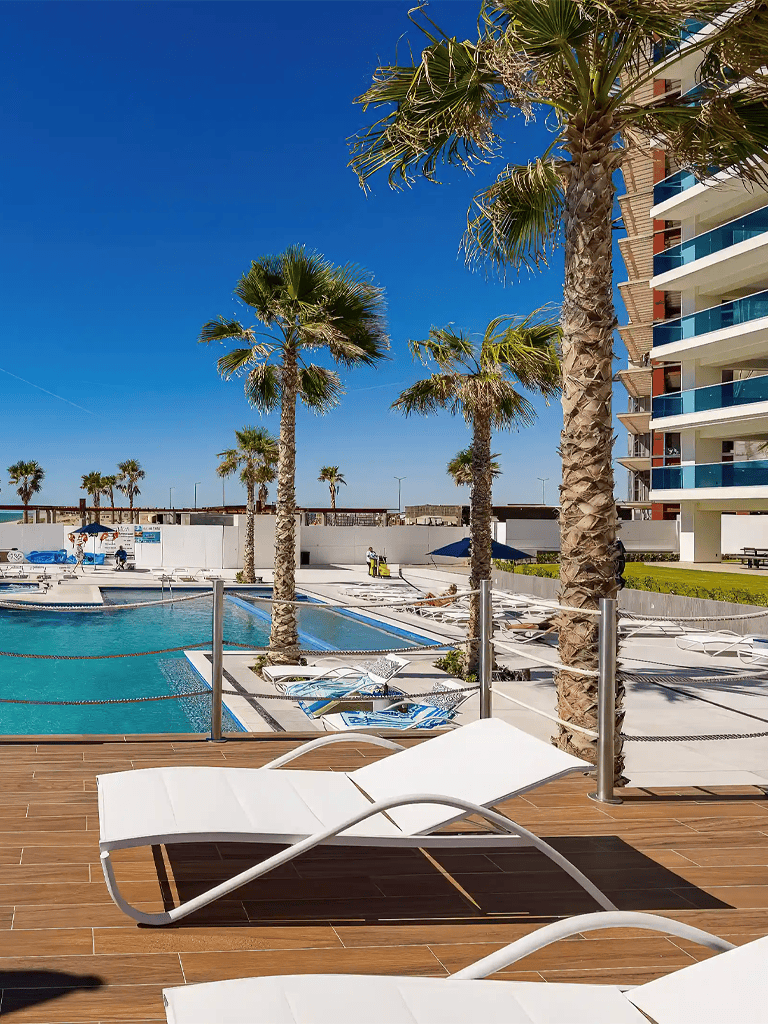 Luxurious poolside with palm trees and modern apartment buildings, perfect for vacation relaxation.