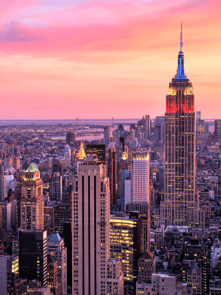 Bright New York City skyline with Empire State Building at sunset, showcasing city lights and vibrant sky.