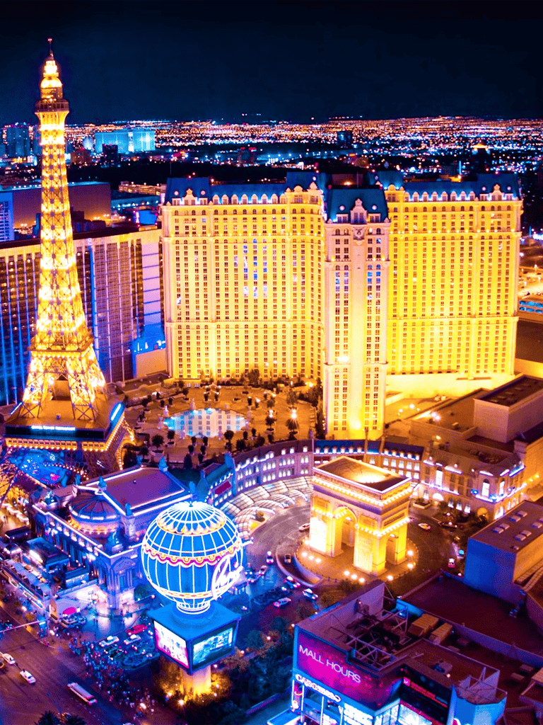 Brightly lit Las Vegas Strip skyline with iconic hotels, casinos, and the Eiffel Tower replica at night.
