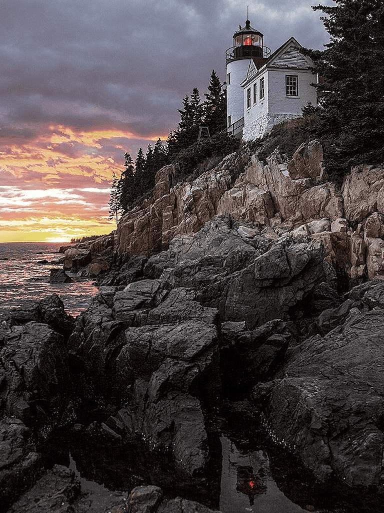 Lighthouse on rocky coast at sunset, scenic coastal view with dramatic sky and ocean.