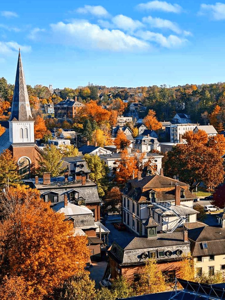 Colorful autumn scenery of a small town with historic buildings and a church steeple, surrounded by fall foliage.