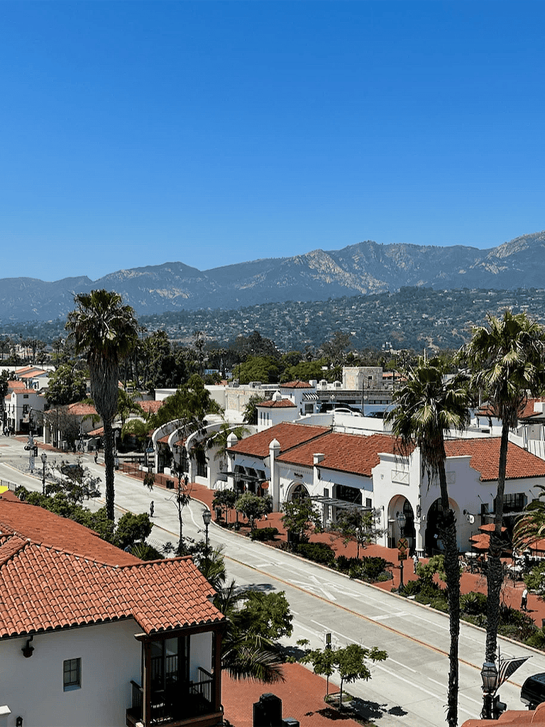 Vibrant streetscape in Santa Barbara with palm trees and Spanish architecture under clear blue sky.