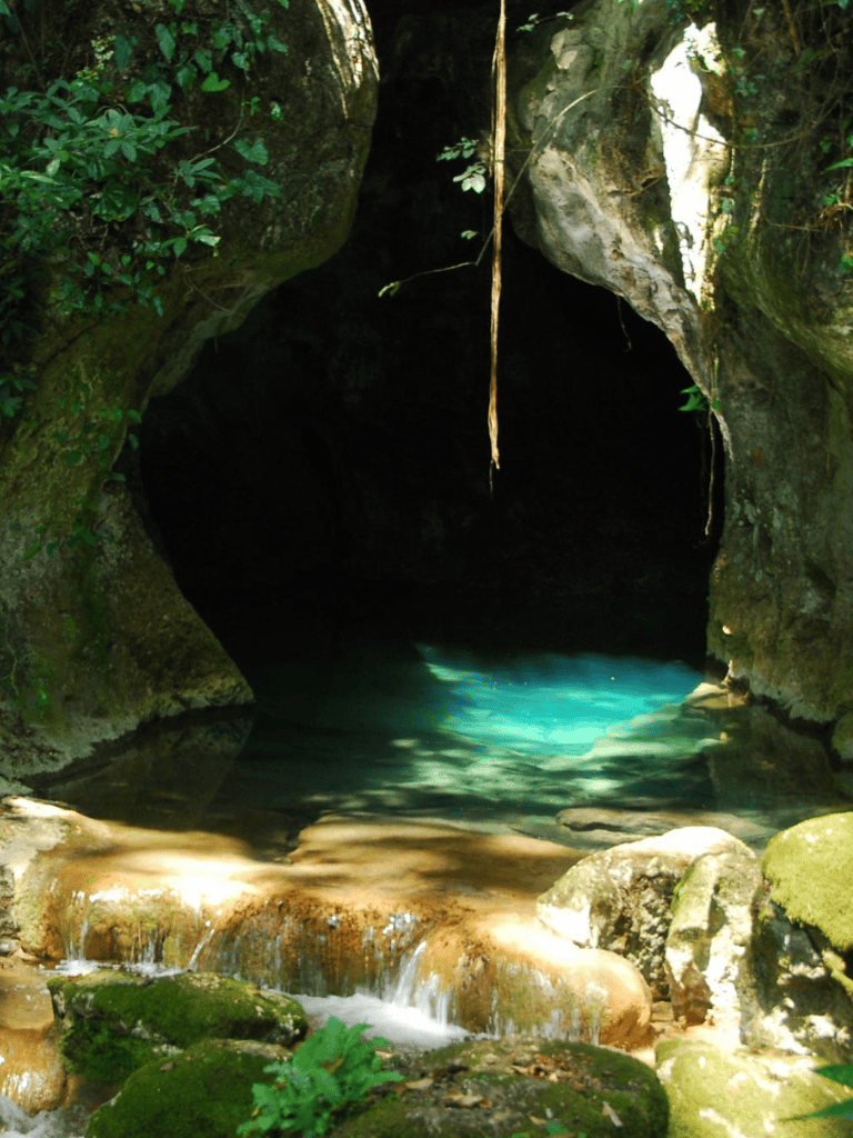 Mysterious cave with turquoise water and lush greenery, perfect for adventure and nature exploration.