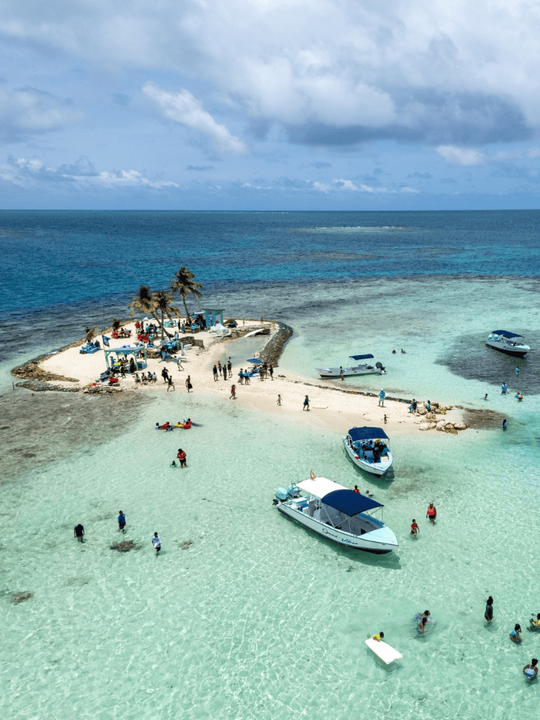 Seaside island with turquoise water, boats, and people enjoying a sunny day on the beach.