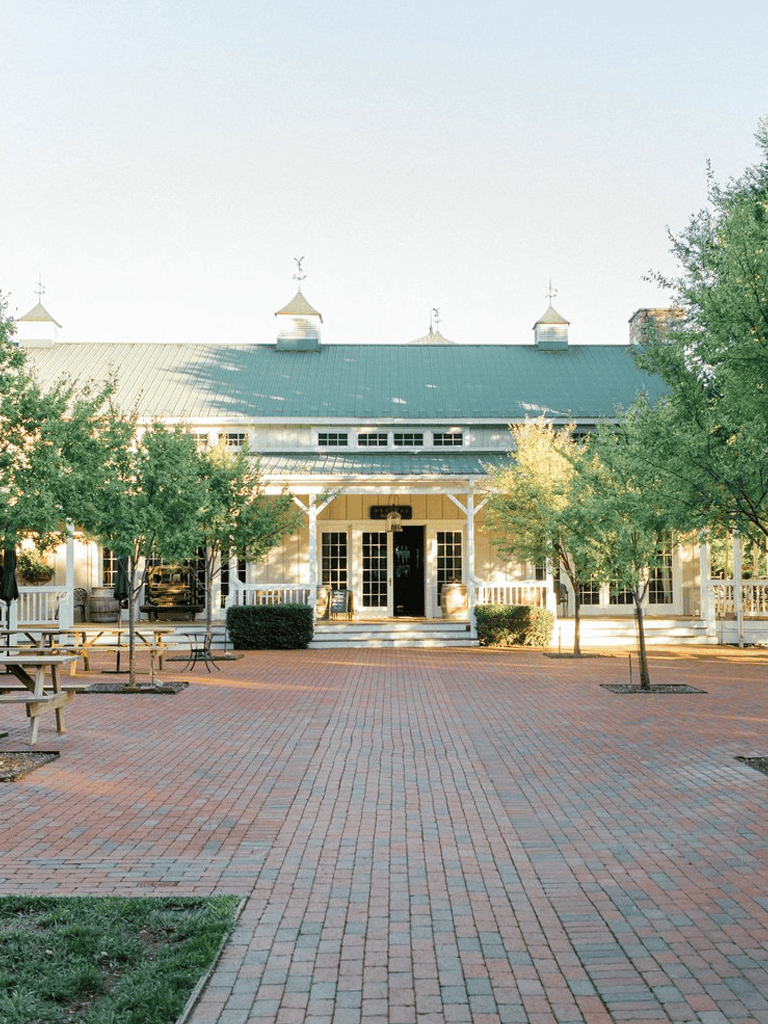 Charming white historic building with green roof, surrounded by trees and outdoor seating area.
