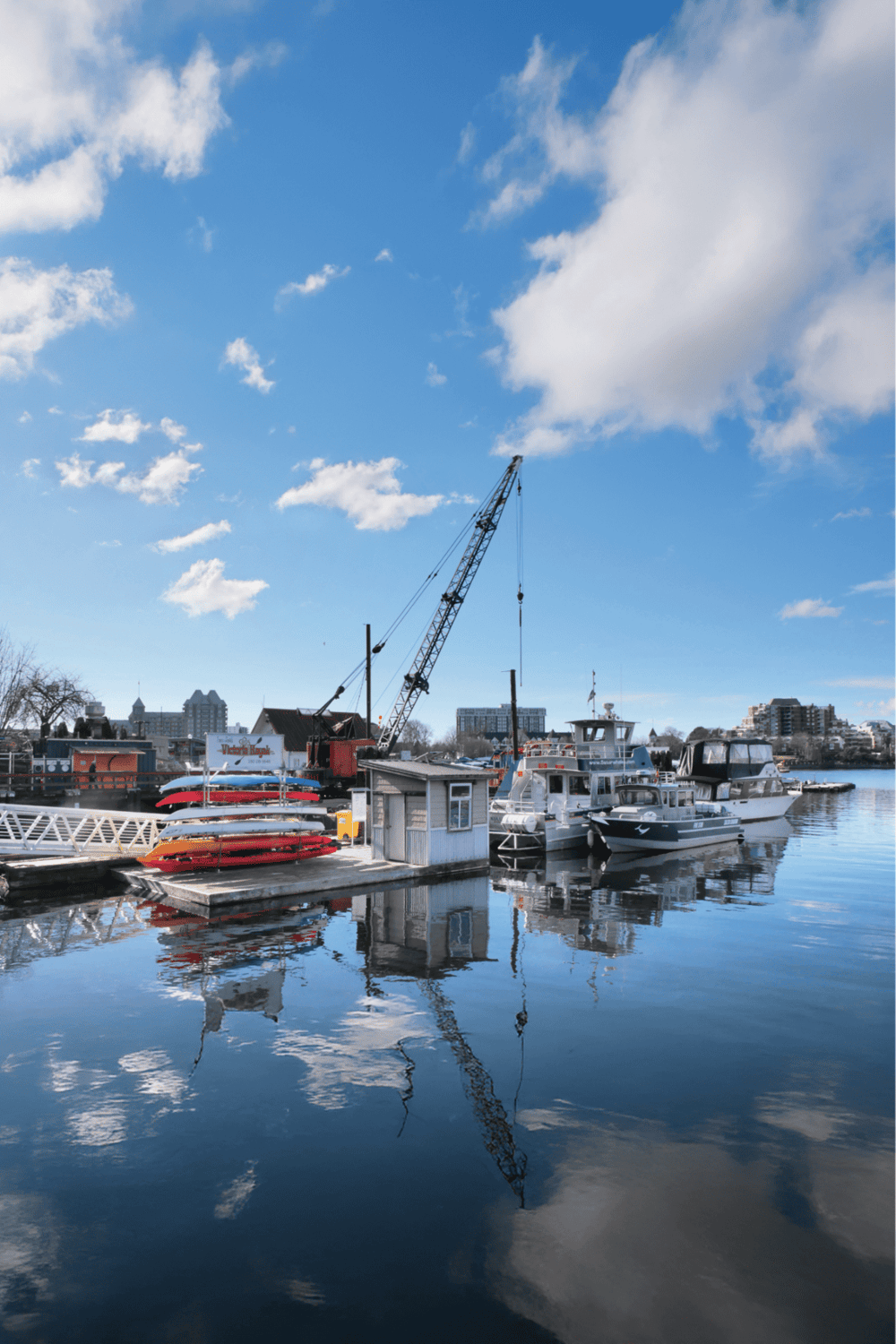 Boats at harbor with crane and city skyline, scenic waterfront view for travel and navigation.