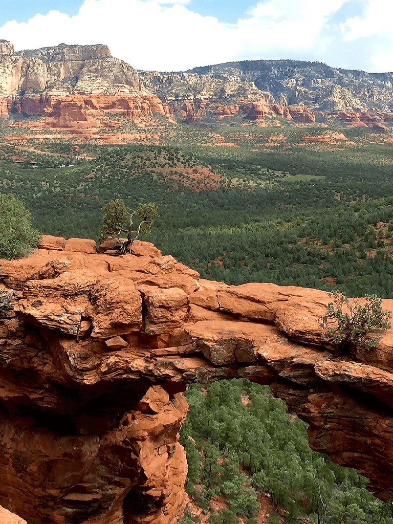 Vibrant red rock arch overlooking lush green desert landscape in Sedona, Arizona.