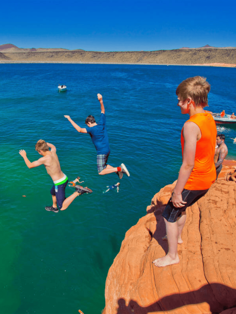 Kids jumping into a lake from a rocky cliff during daytime.