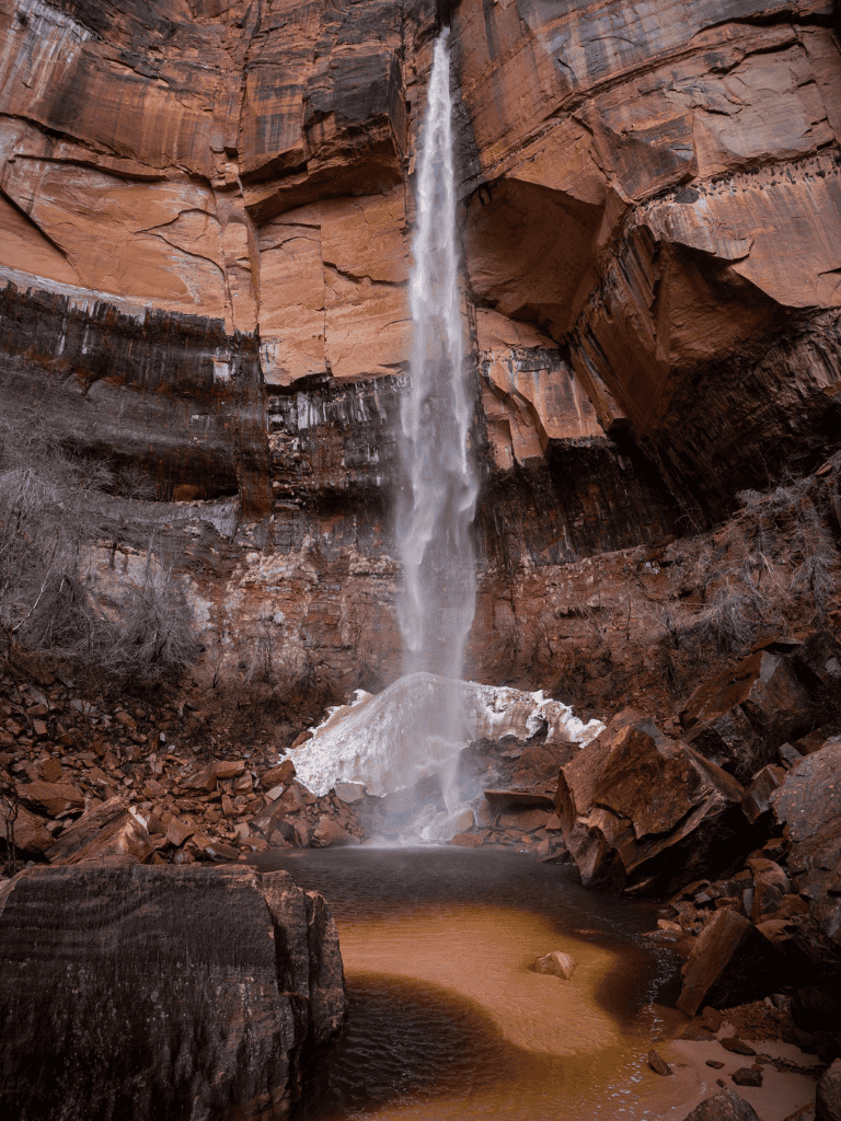 Majestic waterfall cascading down red canyon cliffs, surrounded by rocky terrain and desert landscape.