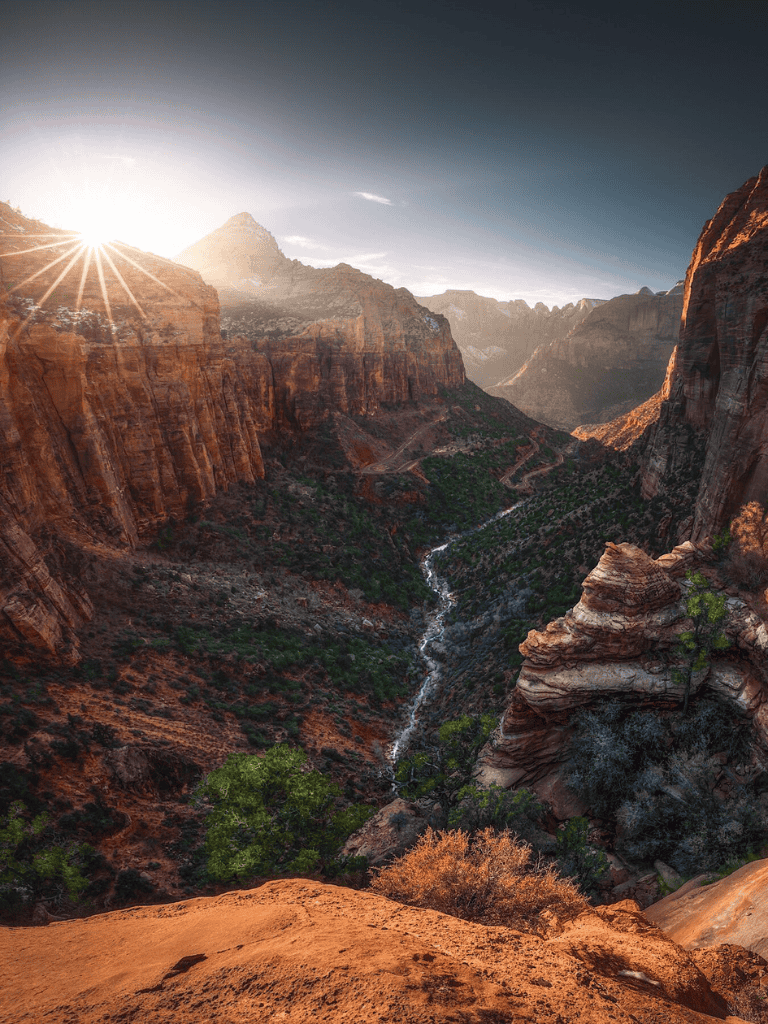 Bright sunset over the Grand Canyon with rugged cliffs and a winding river in the valley.