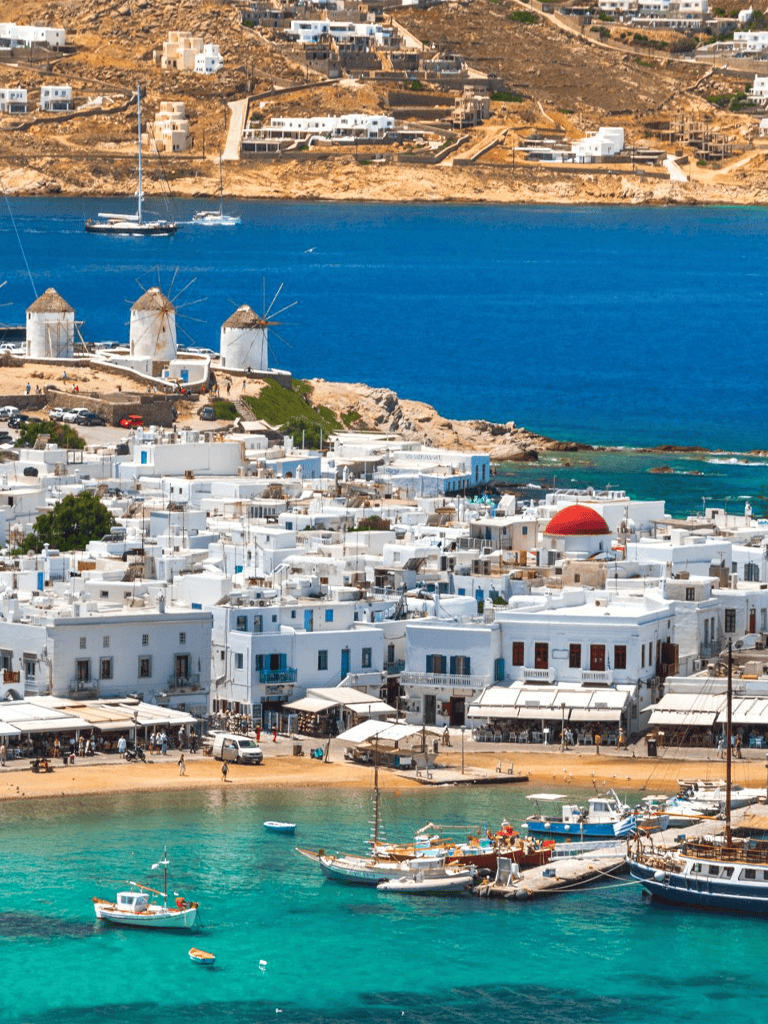 Colorful Mediterranean coastal town with windmills and boats, popular travel destination in Greece.