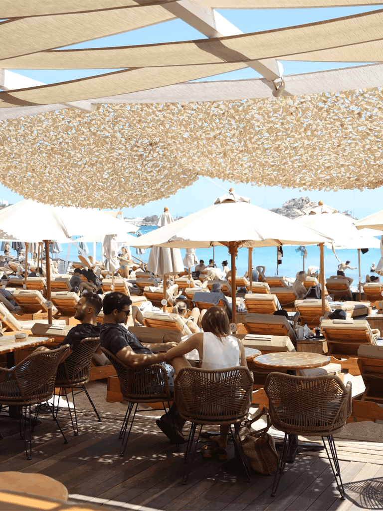 Sunbathers under umbrellas at a beach resort with shaded areas and lounge chairs.
