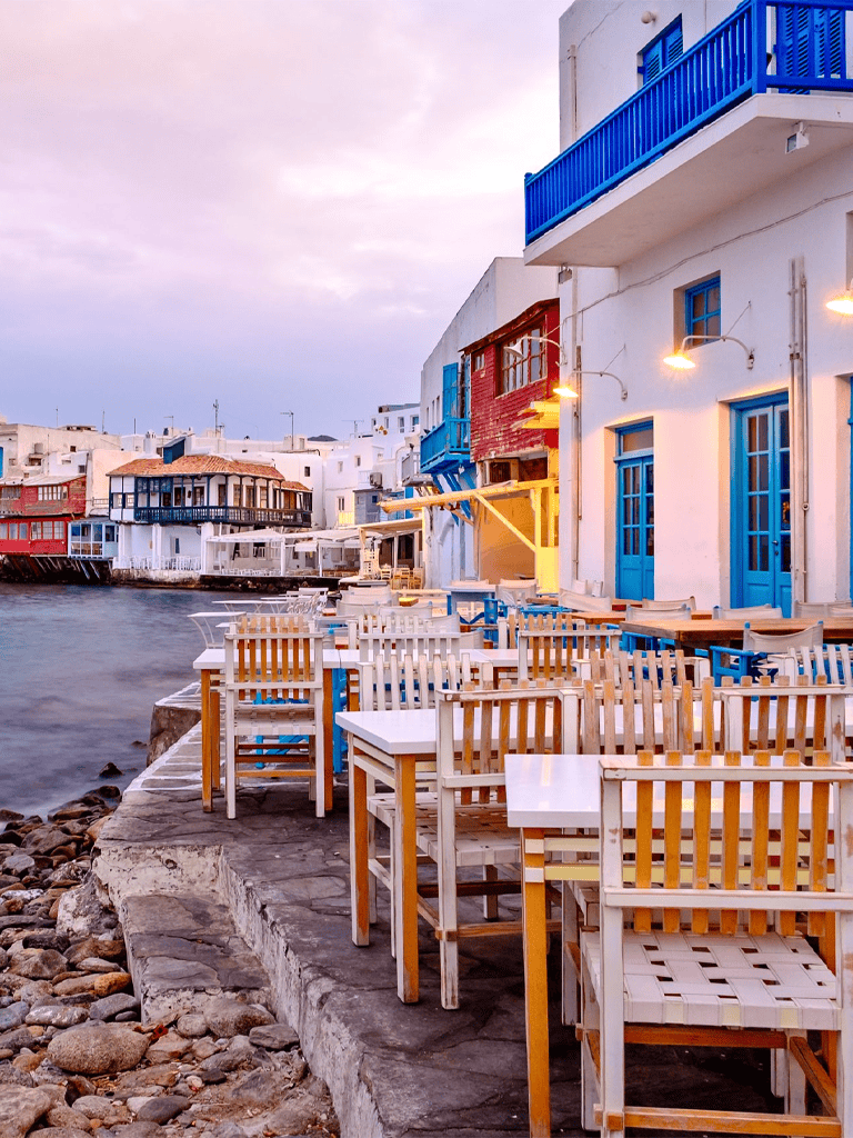 1. Colorful Greek waterfront cafes with blue and red accents along a serene harbor.