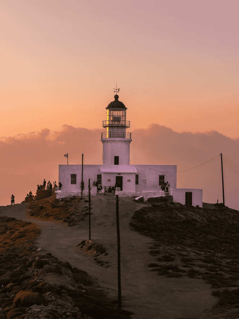 Lighthouse at sunset on coastal cliff with visitors, scenic view, and warm sky.