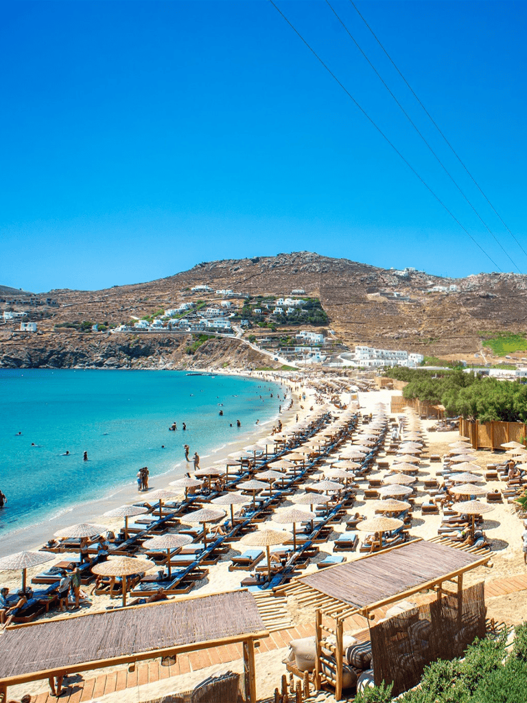 Breathtaking beach view in Santorini showcasing crystal-clear waters, sun loungers, and white-washed buildings on a hillside.