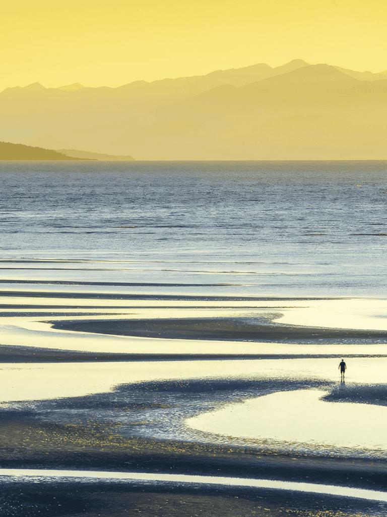Secluded beach with tidal pools at sunset, peaceful coastal landscape and distant mountains.