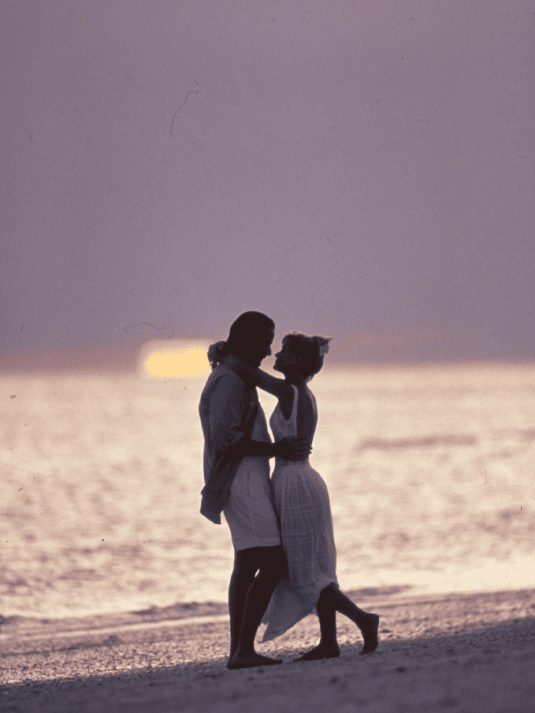 Romantic couple embracing on the beach at sunset, silhouettes, romantic getaway, love, ocean view, evening, travel destination.