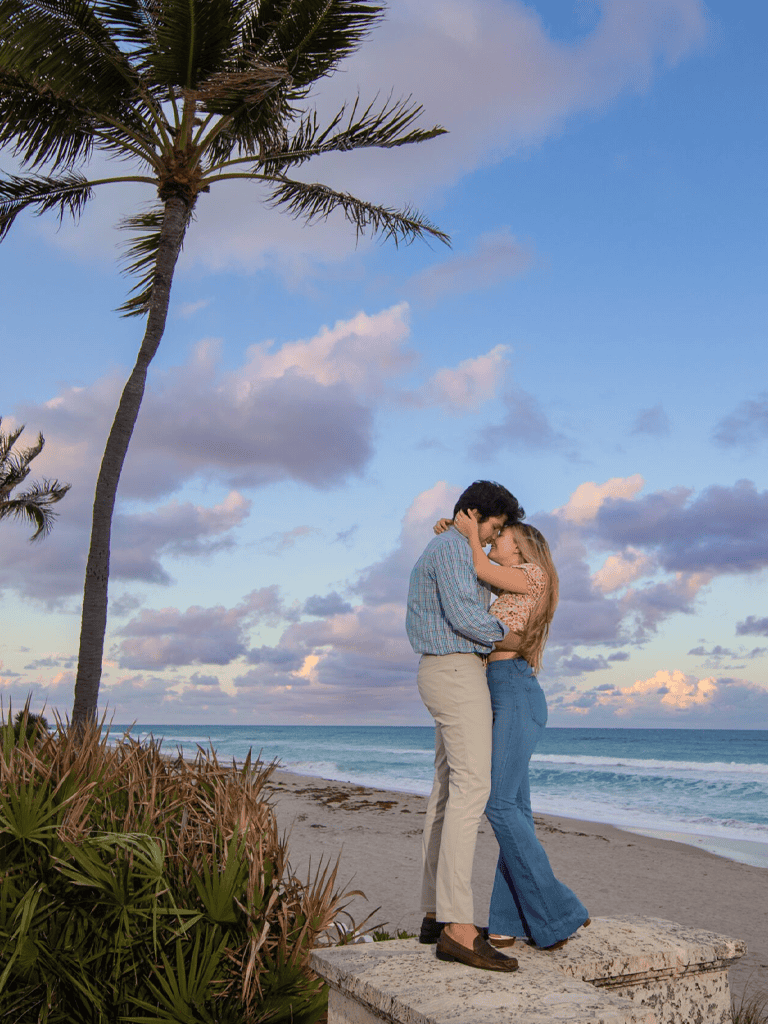 Sunset couple romantic embrace on beach, palm trees, and ocean view for travel and romantic getaway keywords.