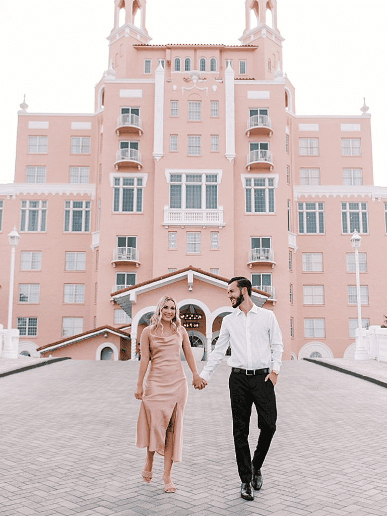 Elegant couple walking in front of pink castle hotel, romantic destination, dream wedding, luxury resort, vacation, sightseeing, travel.