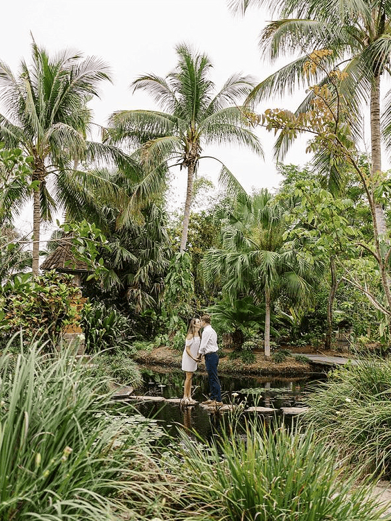Lush tropical garden with palm trees, couple on stepping stones, serene nature scene, romantic outdoor setting, QuestForDirections.